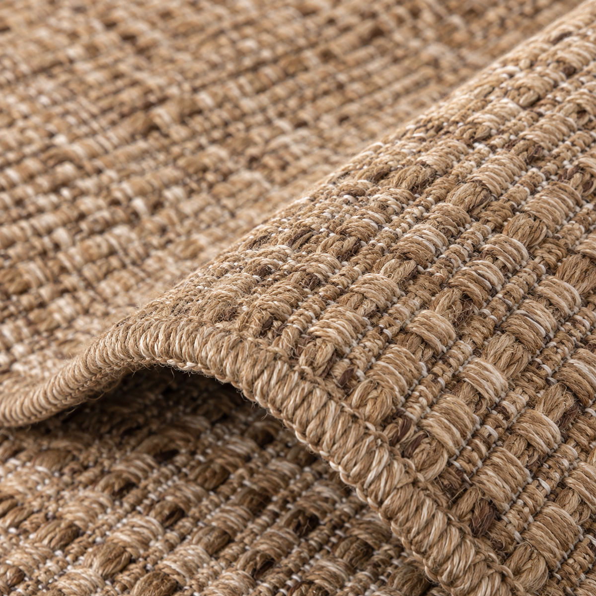 A close-up of a woven natural fiber rug in warm tan and brown tones, with one corner folded over to show the texture and edge.